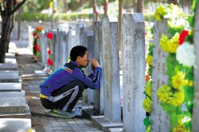 昨日，八宝山人民公墓，一位祭扫的男孩用毛笔为墓碑上的字描新。当日为今年清明第一个祭扫高峰日，5万人到八宝山扫墓。
